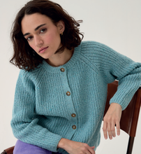 Load image into Gallery viewer, Woman wearing a Sirdar 10780 Loveful 100% Recycled Tweed Double Knit ribbed cardigan sitting on a chair against a white background