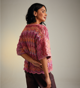 Woman wearing a colourful knitted Sirdar 10715 Jewelspun lace knit cardigan against a plain background