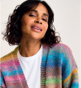 Woman wearing a colourful Sirdar 10801 Jewelspun knitted cardigan over a white shirt against a plain background