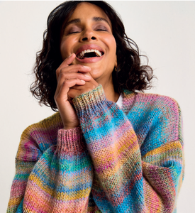 Woman wearing a colourful Sirdar 10801 Jewelspun striped sweater against a plain background